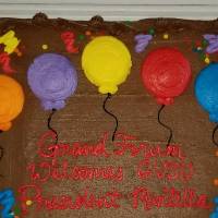 A chocolate cake with frosting balloons and a message that reads "Grand Forum Welcomes GVSU President Mantella"